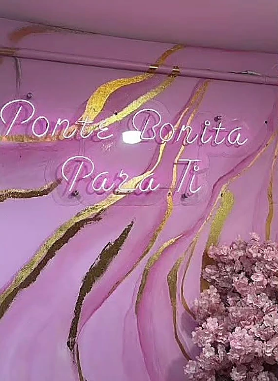 Neón en cursiva que dice Ponte bonita para ti sobre el muro rosa con vetas doradas y flores