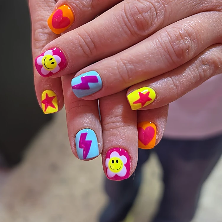 Uñas cortas con caritas sonrientes, rayos, estrellas y corazones en amarillo, rosa, naranja y azul