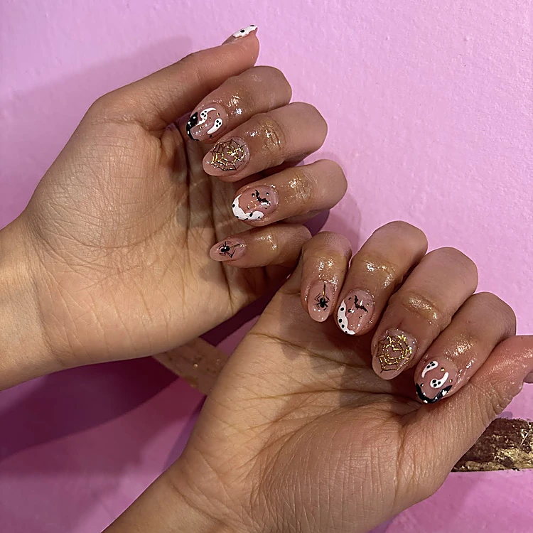 Uñas nude de Halloween con fantasmas blancos, arañas y telarañas doradas sobre el muro rosa