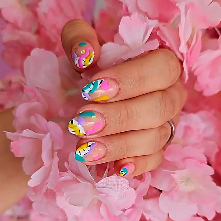 Uñas cortas con flores en colores pastel sobre base nude, entre flores rosas