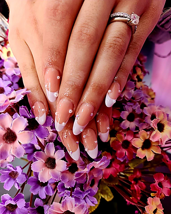Francesas blancas finas en uñas almendradas largas con puntos blancos, sobre flores moradas