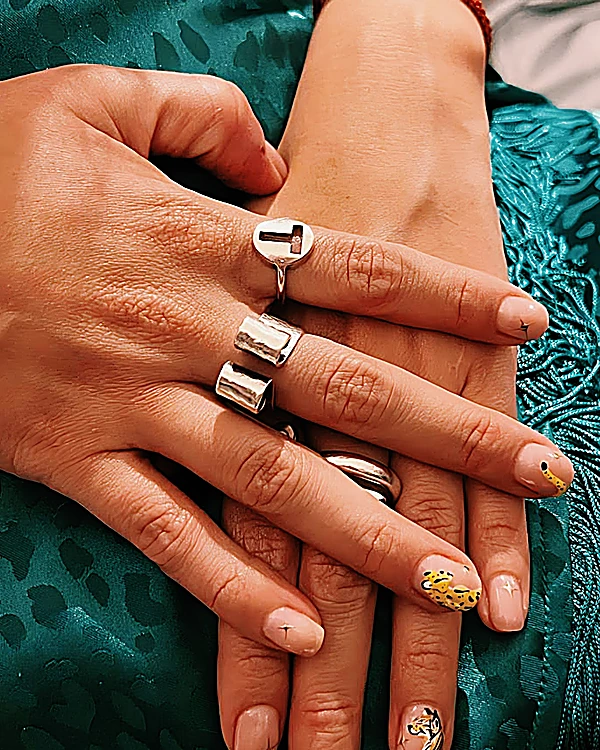 Uñas nude con pequeños dibujos dorados y negros, manos con anillos plateados